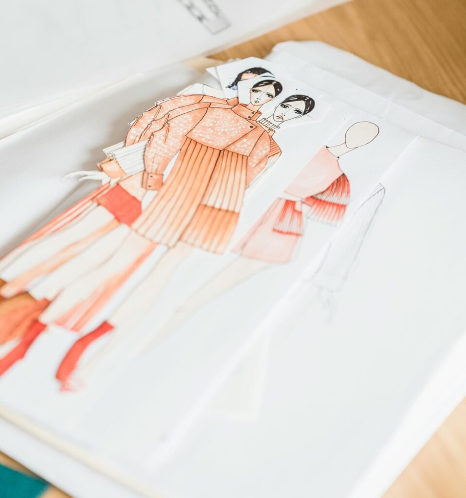 Colorful creative drafts of stylish garments placed on white paper on wooden table with patterns and drafts in modern workshop