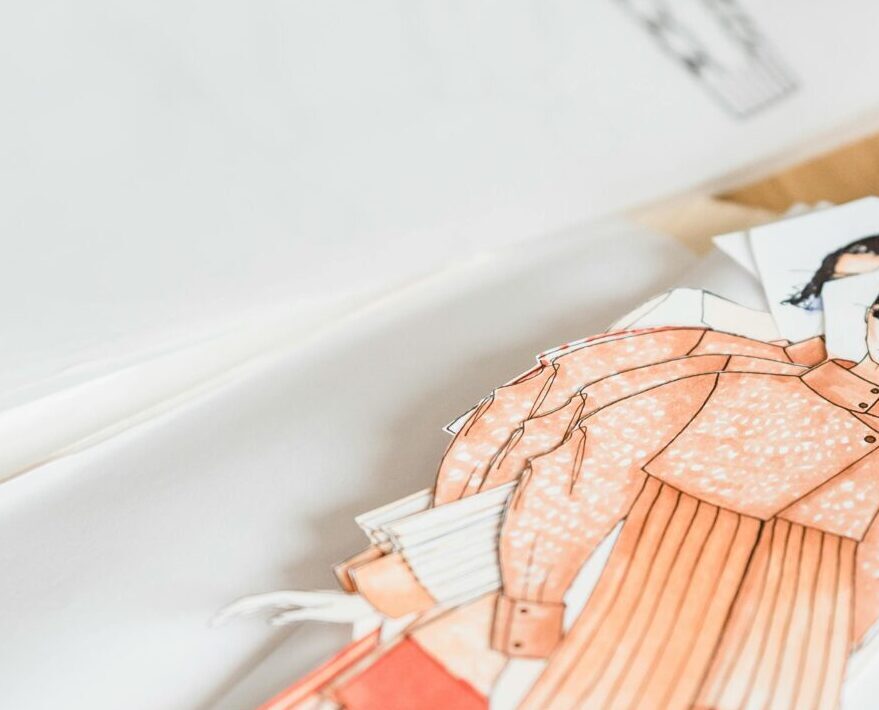 Colorful creative drafts of stylish garments placed on white paper on wooden table with patterns and drafts in modern workshop